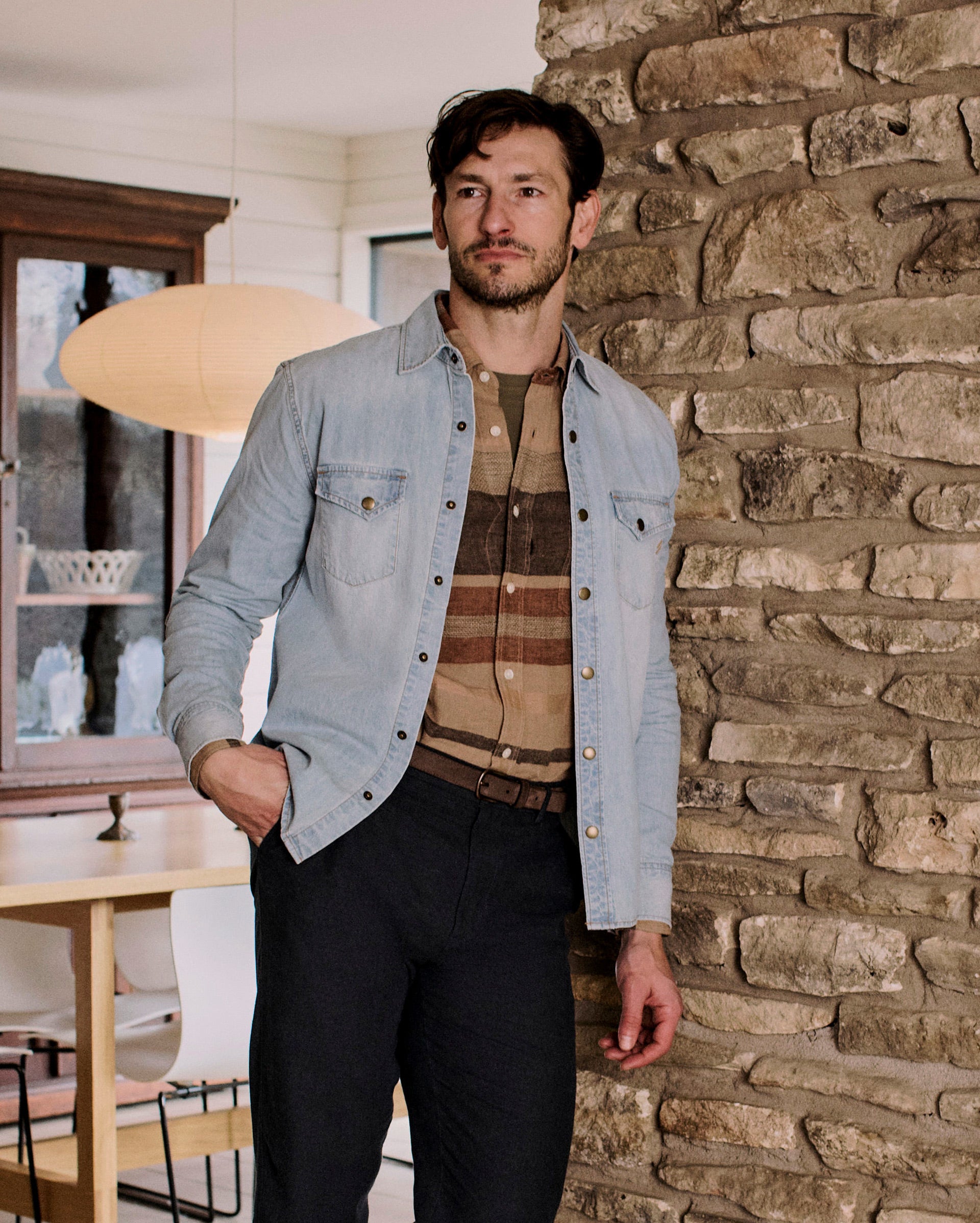 Man standing against a stone wall in a room with furniture and decor.
