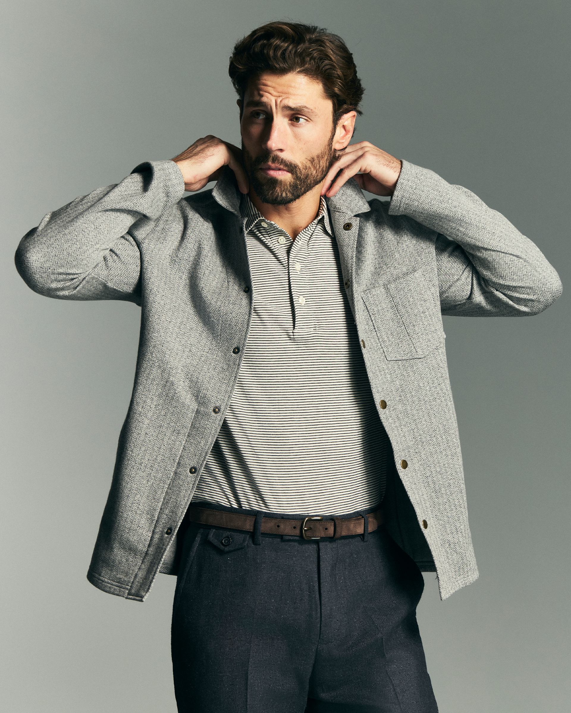 Man wearing a gray jacket over a striped shirt on a gray background
