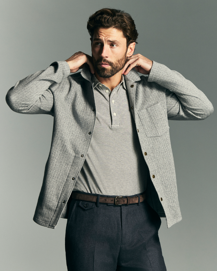 Man wearing a gray jacket over a striped shirt on a gray background