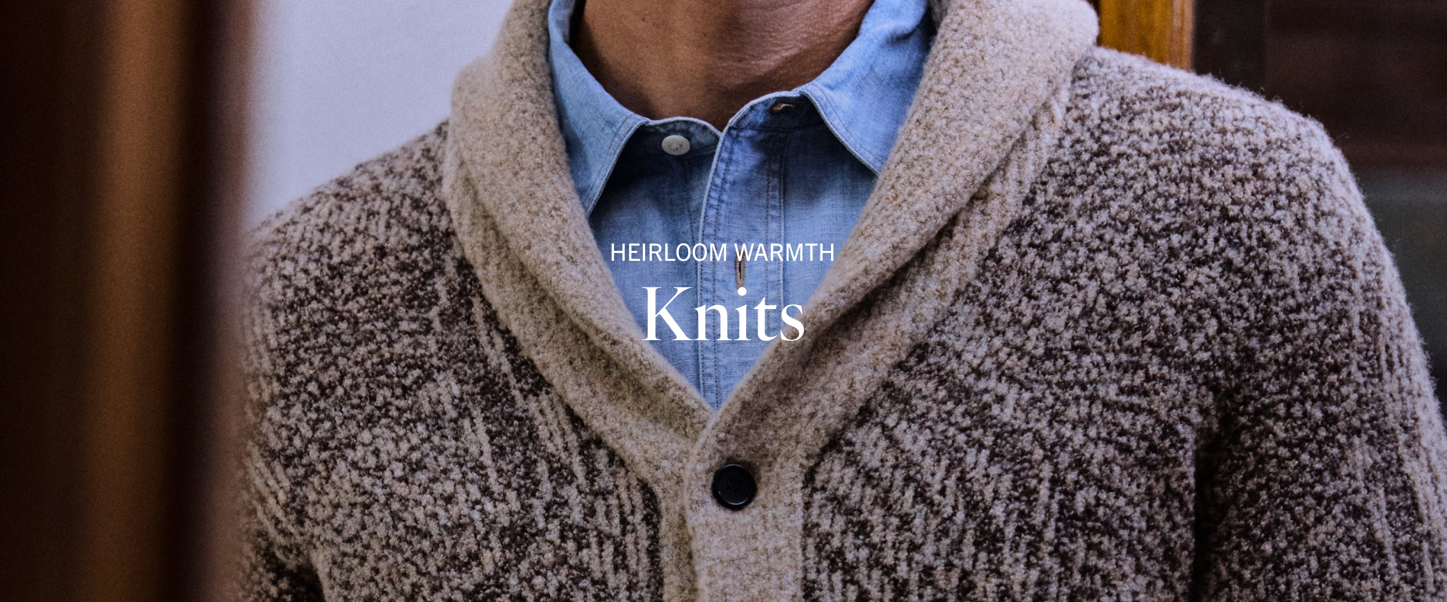 Person wearing a brown knitted cardigan over a blue shirt with 'Heirloom Warmth Knits' text.