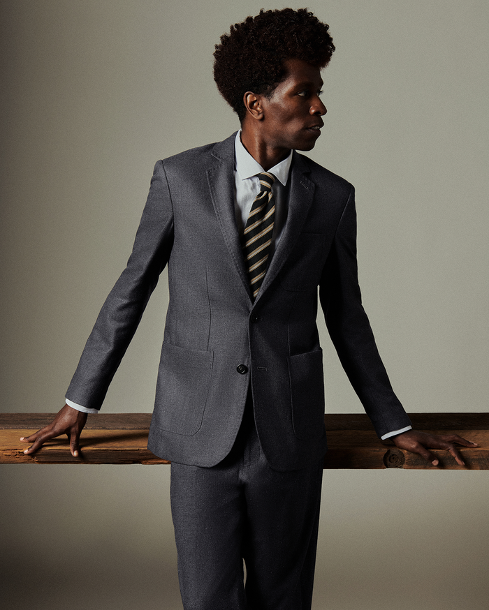 Man in a gray suit with a striped tie leaning against a wooden surface.
