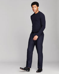 A man modeling a dark navy blue knit sweater and matching navy trousers with black dress shoes, standing against a light gray studio background.