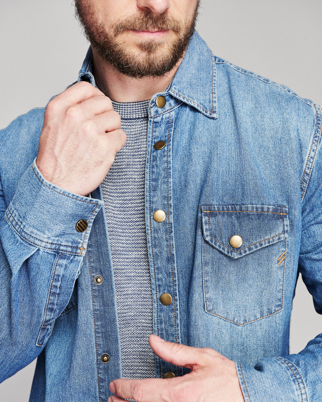 Model adjusts the collar of a denim shirt.