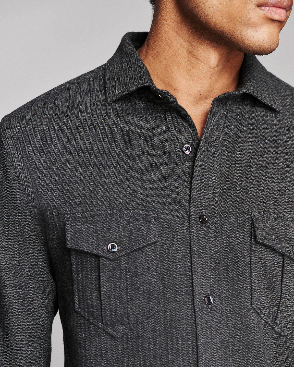 Close-up of a man wearing a dark charcoal gray textured button-down shirt with two chest pockets and silver buttons.