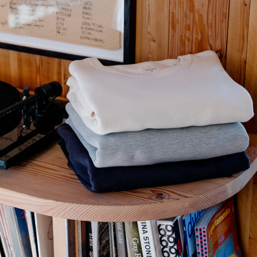 Stack of folded clothes on a wooden shelf with vinyl records below