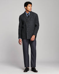 A man modeling a dark gray double-breasted wool-blend blazer with matching gray trousers, a light blue dress shirt, a dark tie, and black loafers, photographed against a neutral light gray studio background.