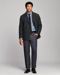 A man modeling a dark charcoal gray double-breasted blazer with matching gray trousers, a light blue dress shirt, a dark tie, and black dress shoes, photographed against a neutral light gray studio background.