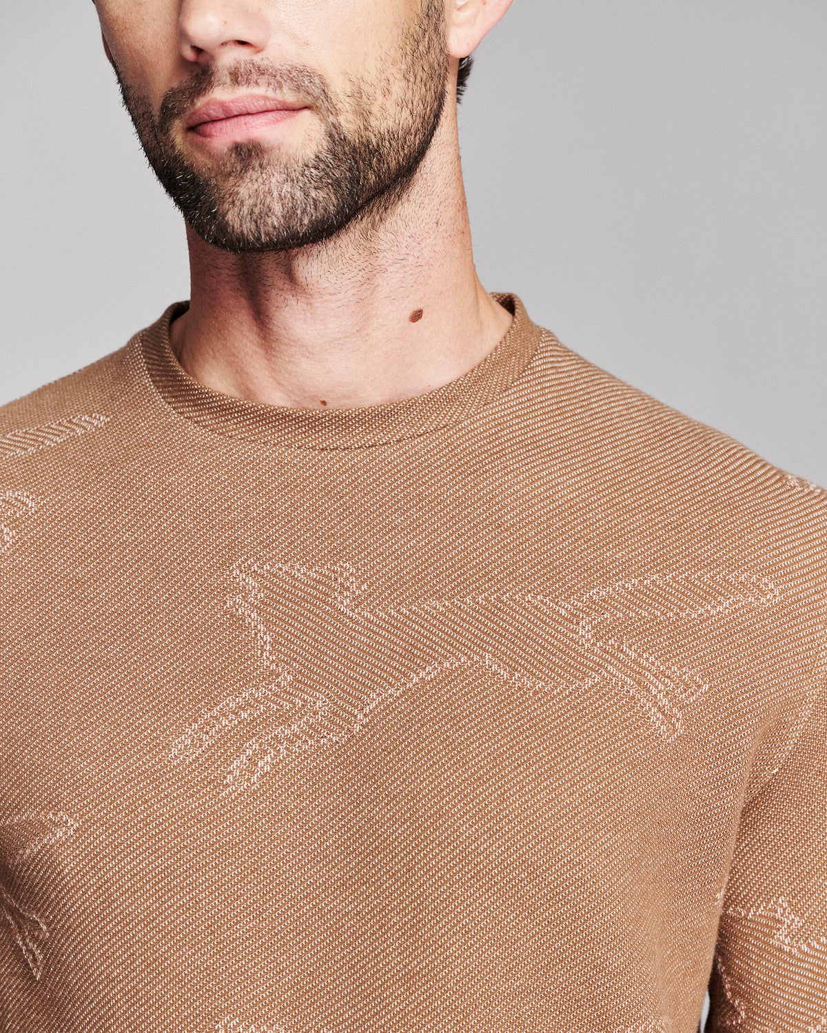 Close-up of a man wearing a brown knit crewneck sweater with a subtle tonal jacquard pattern.