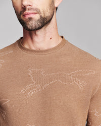 Close-up of a man wearing a brown knit crewneck sweater with a subtle tonal jacquard pattern.