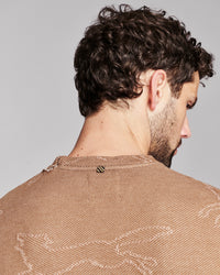Close-up back view of a man with curly dark hair wearing a textured tan knit top against a light gray studio background.