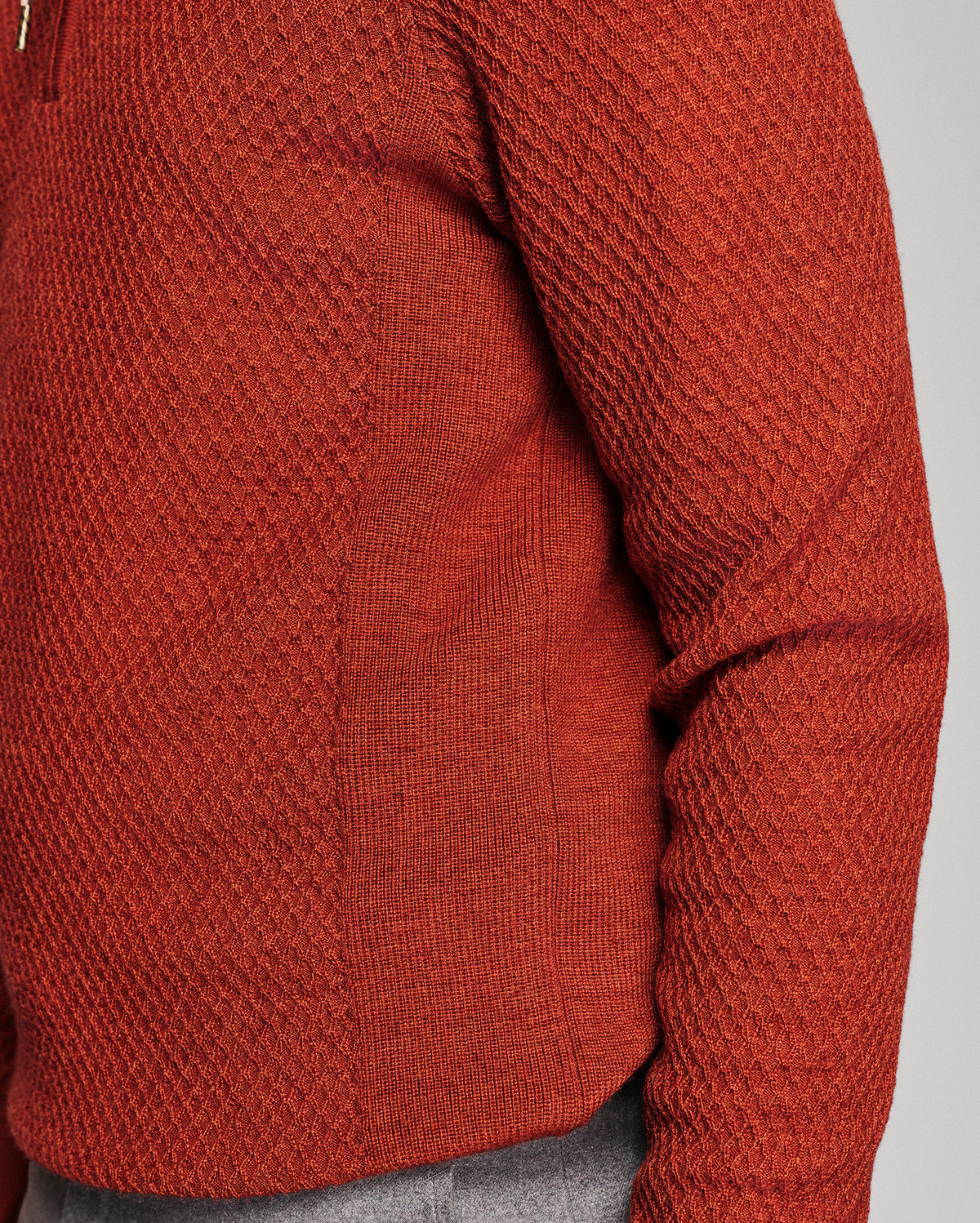 Close-up of a textured knit sweater in a rust-orange color, showing the detailed ribbed and waffle-knit patterns on the torso and sleeve.