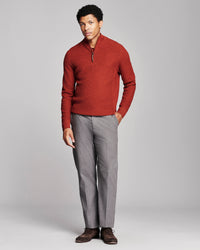 A man modeling a textured rust-red quarter-zip sweater and gray trousers against a light gray studio background.