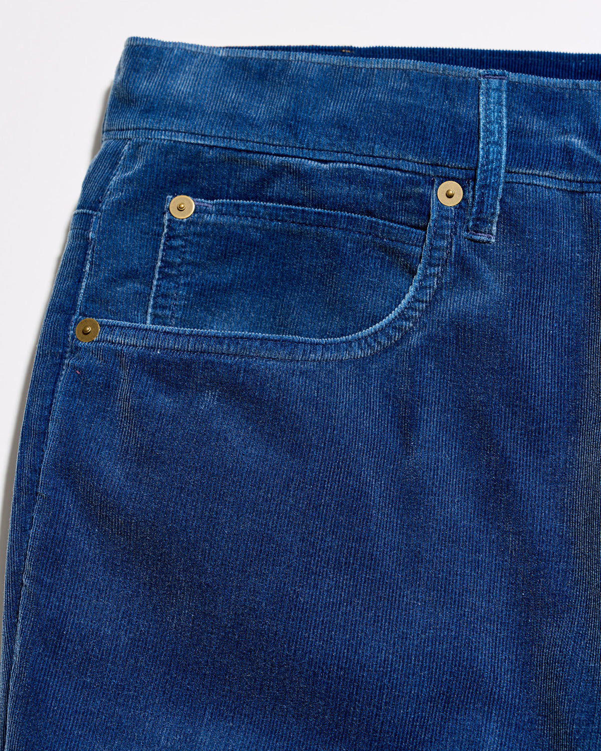 Close-up of a pair of blue corduroy jeans showing the front pocket, button, and rivet details.