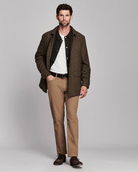 A man modeling a brown textured overshirt over a black button-up shirt and white tee, paired with tan trousers and dark brown leather shoes, against a solid gray studio background.