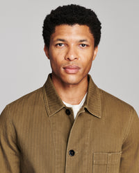 A man wearing a brown corduroy button-up shirt over a white undershirt, photographed against a solid gray background.