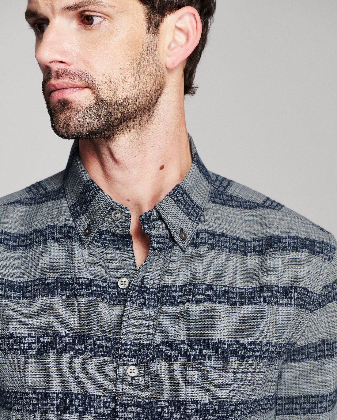 A close-up of a man wearing a blue and gray striped button-down shirt with a subtle geometric pattern.