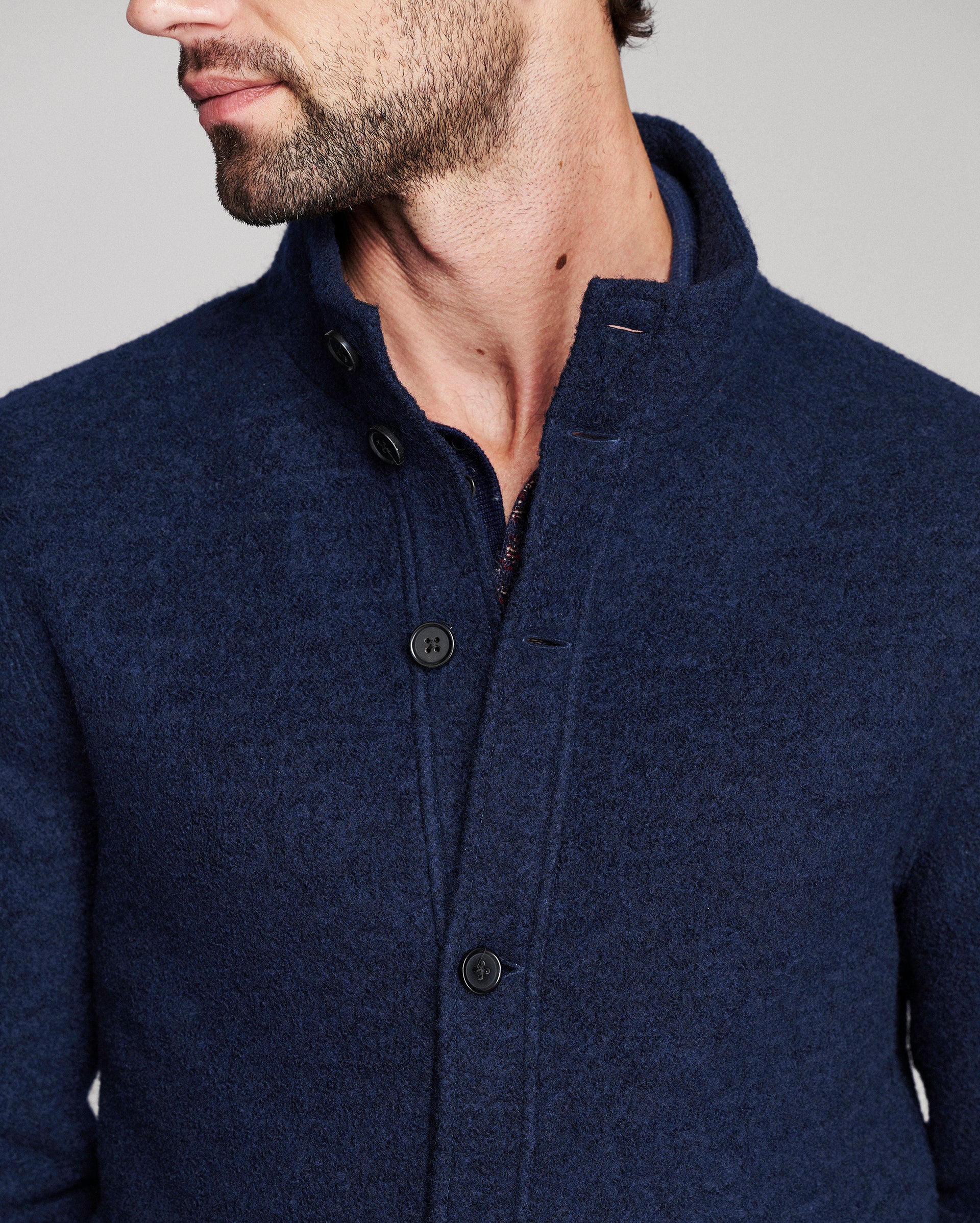 Close-up of a man wearing a dark navy blue textured wool-blend cardigan sweater with a high collar and dark buttons.