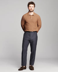 A man modeling a textured brown long-sleeve polo shirt, dark gray trousers, and brown suede loafers against a light gray studio background.