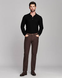 A man modeling a black long-sleeve knit polo shirt and brown trousers against a solid gray studio background.