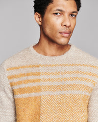 A close-up of a man wearing a fuzzy knit crewneck sweater with horizontal stripes in beige, yellow, and white.