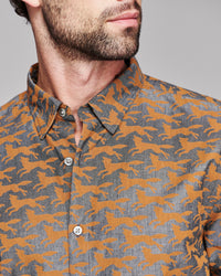 Close-up of a man wearing a button-down shirt with an allover orange fox pattern on a heather gray background.