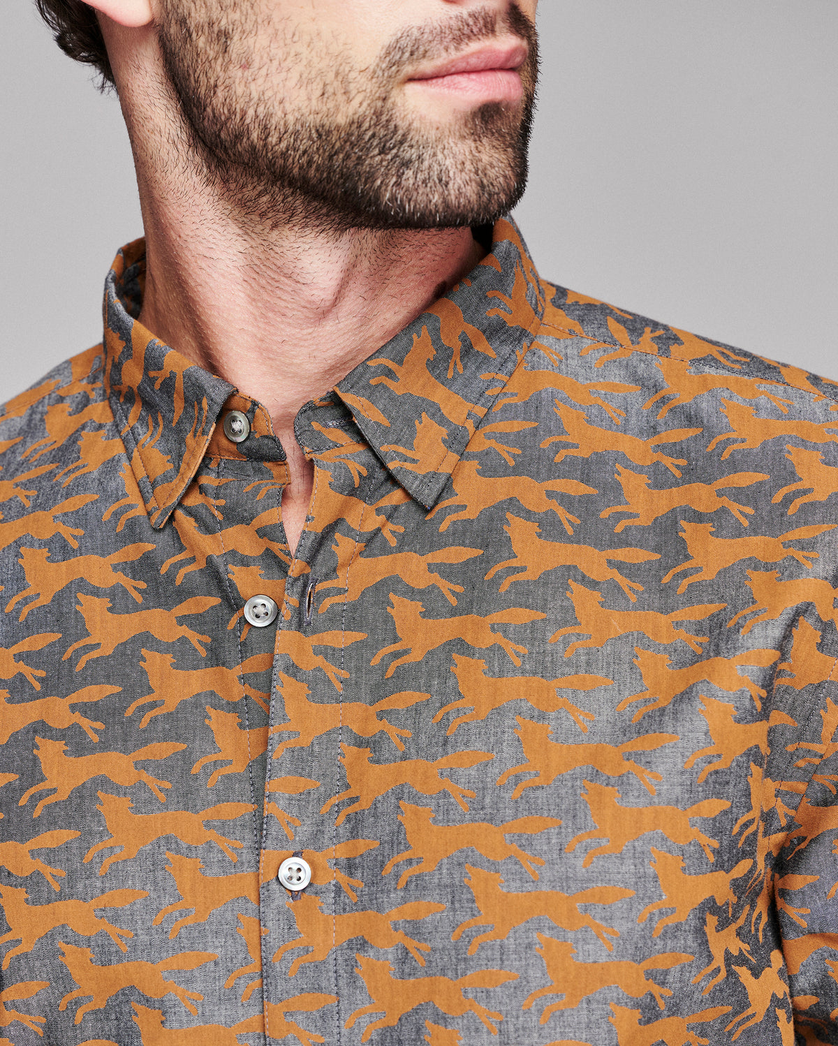 Close-up of a man wearing a button-down shirt with an allover orange fox pattern on a heather gray background.
