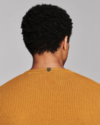 Back view of a person with curly black hair wearing a textured mustard yellow knit sweater against a solid gray background.