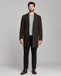 A man modeling a dark brown and black micro-check blazer over a light blue knit sweater, black trousers, and brown leather shoes, shot against a solid gray studio background.