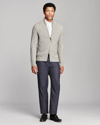 A man modeling a light gray textured knit cardigan over a white collared shirt, paired with dark blue trousers and black loafers, against a solid gray studio background.