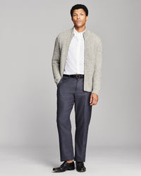 A man modeling a light gray textured knit cardigan over a white collared shirt, paired with navy blue trousers and black dress shoes, against a solid light gray studio background.