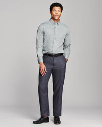 A man modeling a light gray and white chevron-patterned button-down shirt with dark gray trousers, a black belt, and black dress shoes, standing against a light gray studio background.