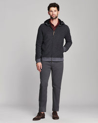 A man modeling a dark gray zip-up hoodie with a ribbed hem and cuffs, worn over a burgundy shirt and paired with dark gray trousers and brown suede shoes, against a light gray studio background.