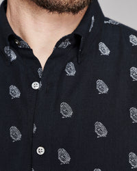 Close-up of a man wearing a black button-up shirt with a repeating white embroidered owl pattern.