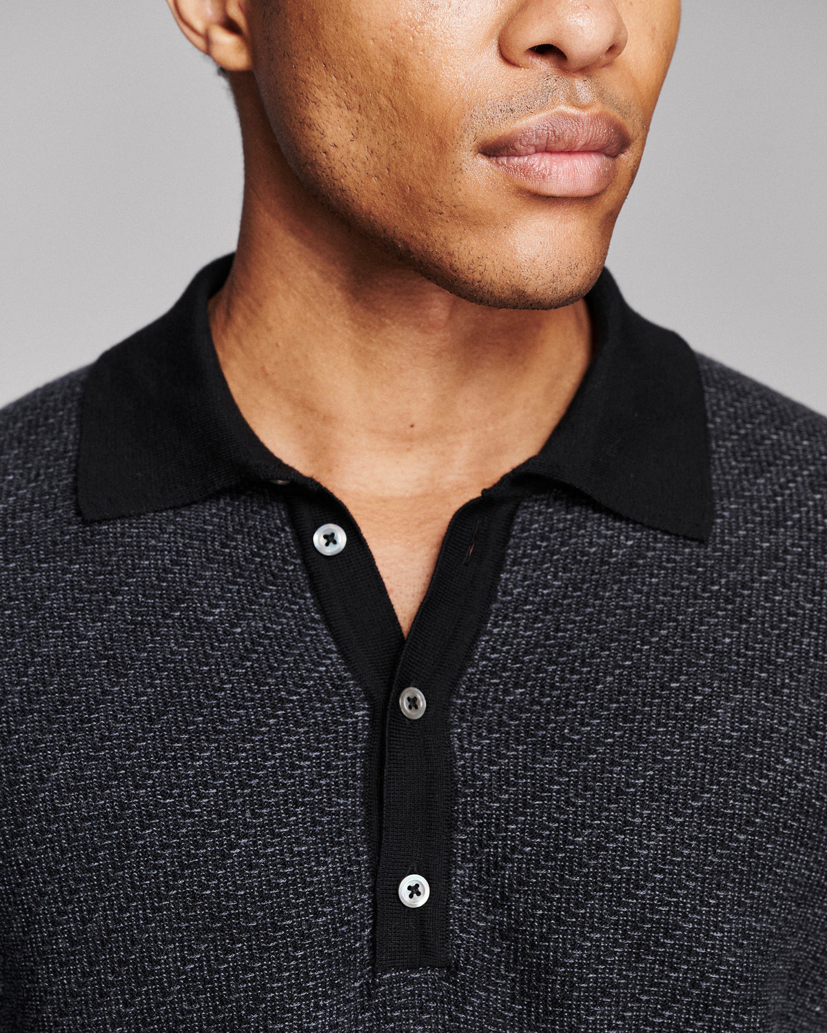 Close-up of a man wearing a dark charcoal and black textured polo shirt with a solid black collar and three-button placket.