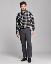 A man modeling a black and white plaid button-down shirt with dark gray trousers and black dress shoes, standing against a solid gray studio background.