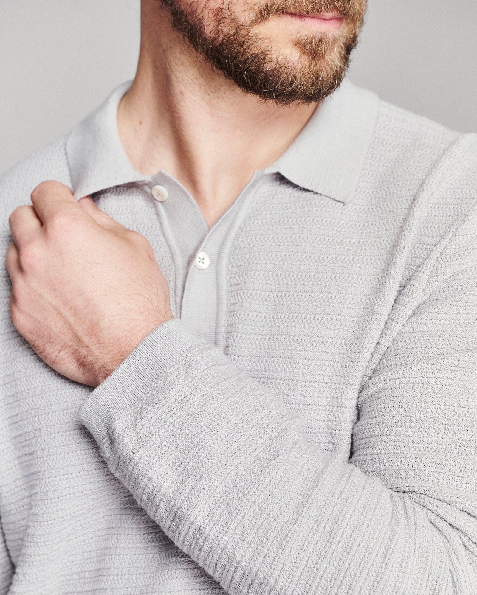 Close-up of a man wearing a light gray ribbed knit polo shirt, showing the collar, buttons, and textured fabric on his chest and arm.