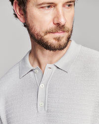 Close-up of a man wearing a light gray textured knit polo shirt against a neutral gray background.