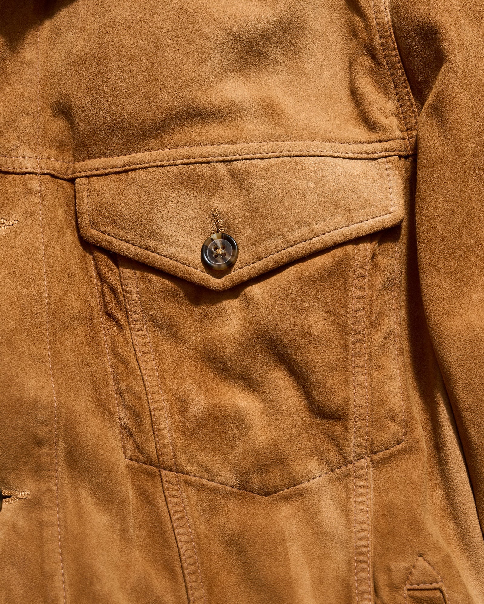 Close-up of a brown leather jacket with a pocket and button.