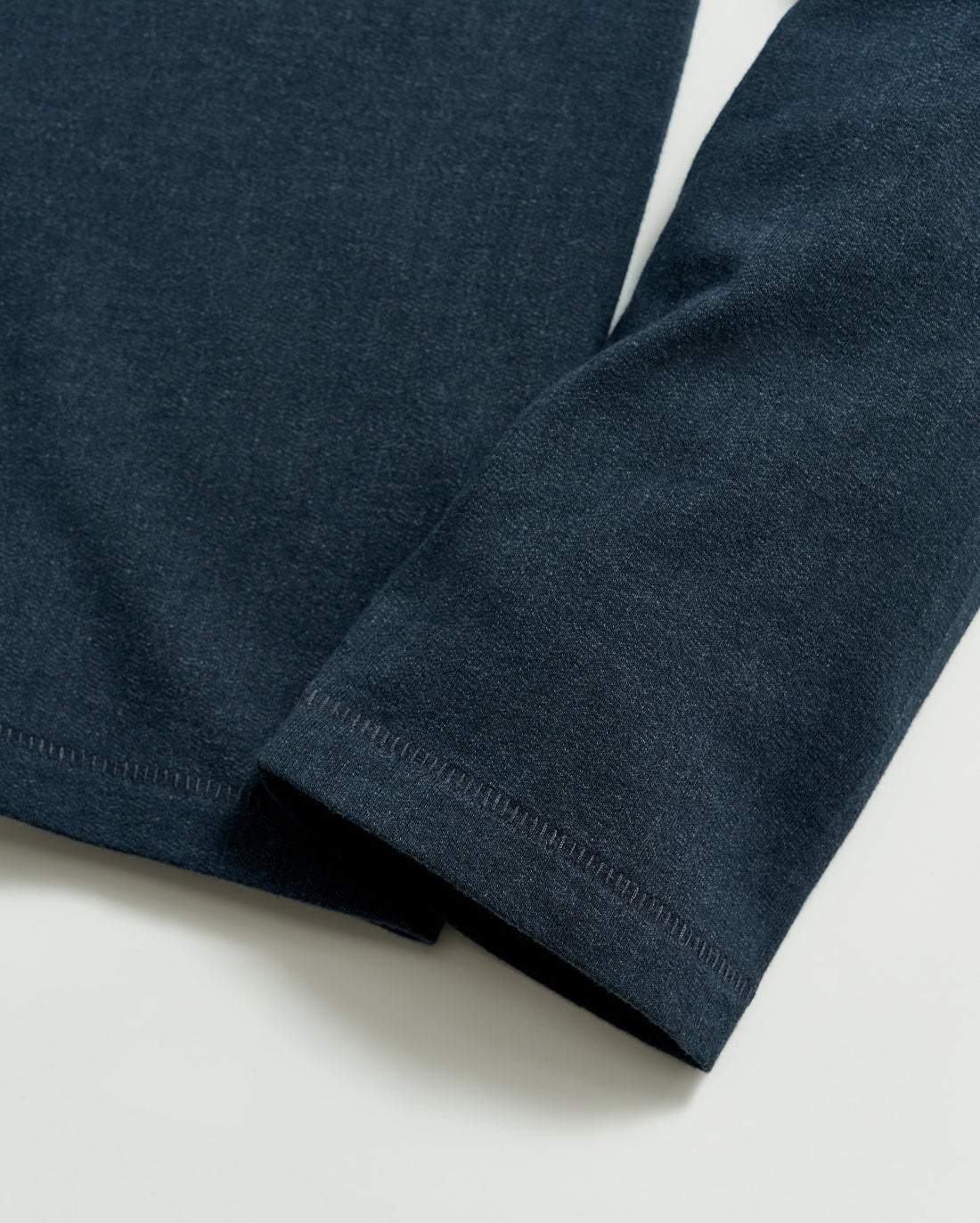 A close-up of a dark blue long-sleeve shirt sleeve laying flat on a light surface, showing the fabric texture and stitching detail at the cuff and hem.