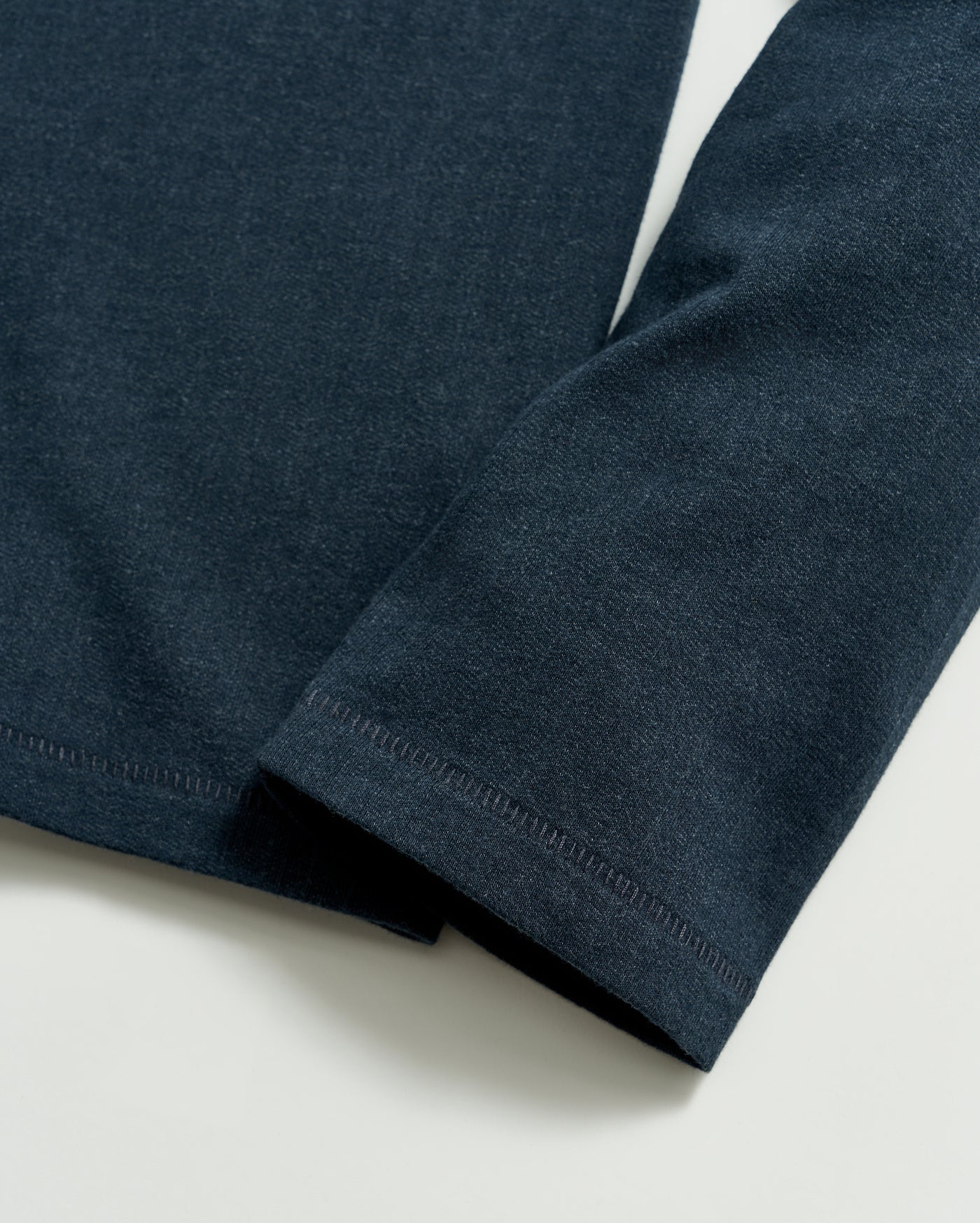 A close-up of a dark blue long-sleeve shirt sleeve laying flat on a light surface, showing the fabric texture and stitching detail at the cuff and hem.