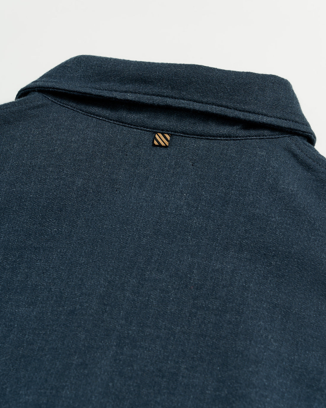 Close-up of the back of a dark blue collared shirt, showing a small, striped loop detail just below the collar on a plain white background.