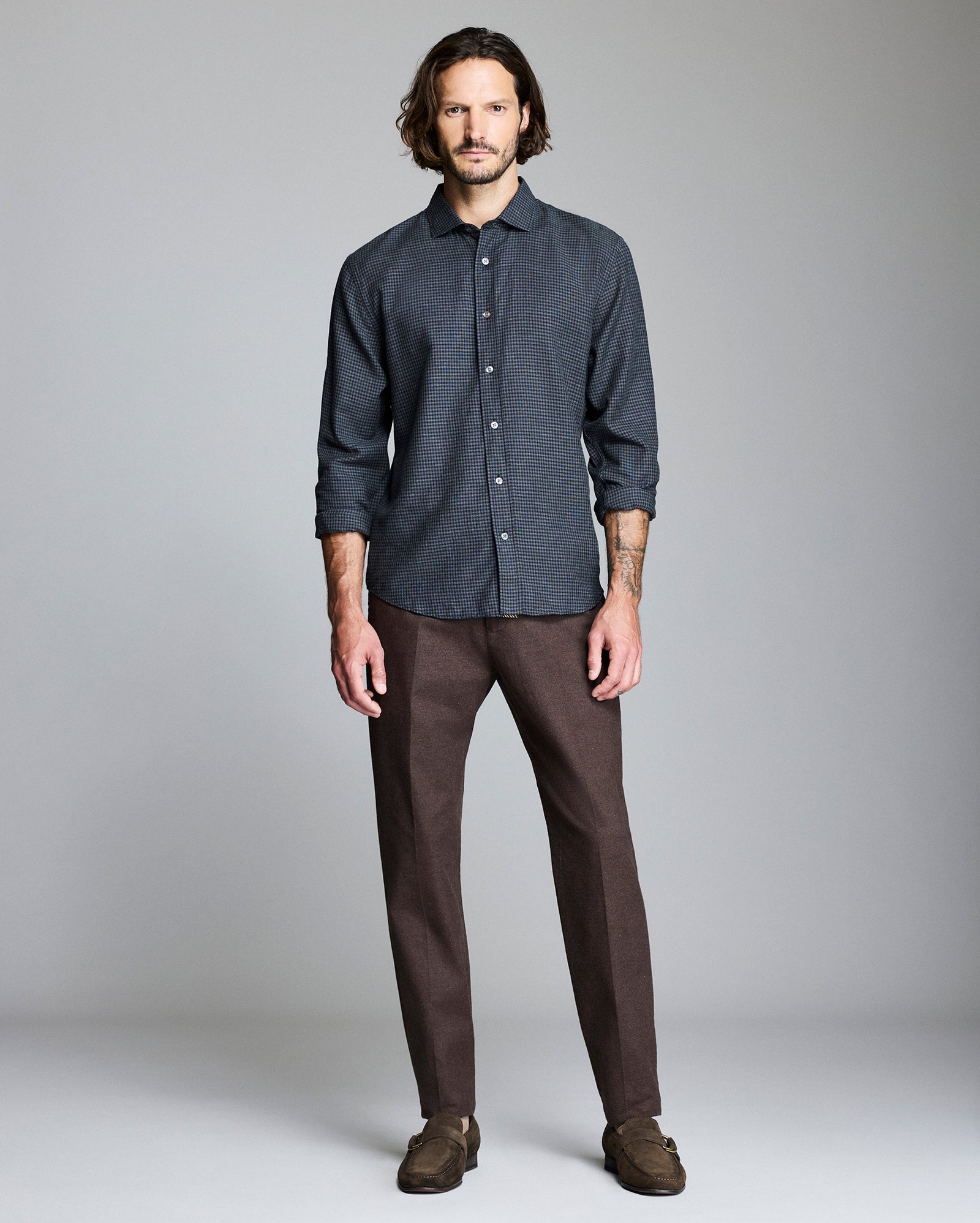 Man wearing a dark patterned shirt and brown pants against a gray background