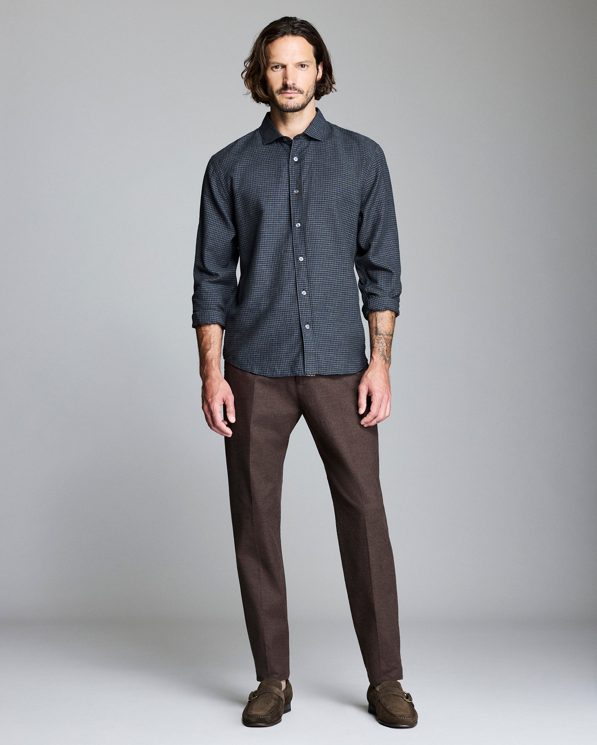 Man wearing a dark patterned shirt and brown pants against a gray background