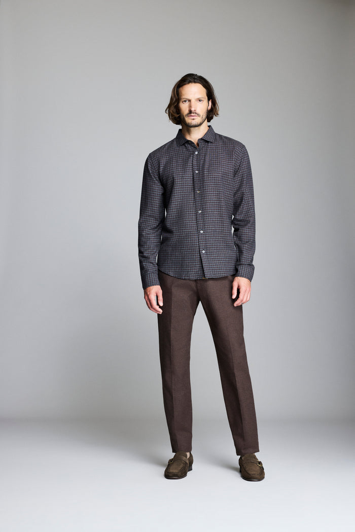 Man wearing a dark checkered shirt and brown pants against a gray background