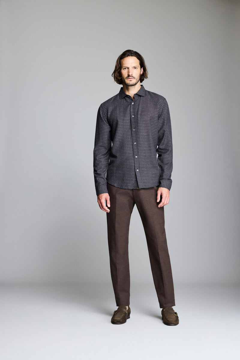 Man wearing a dark checkered shirt and brown pants against a gray background Alternate