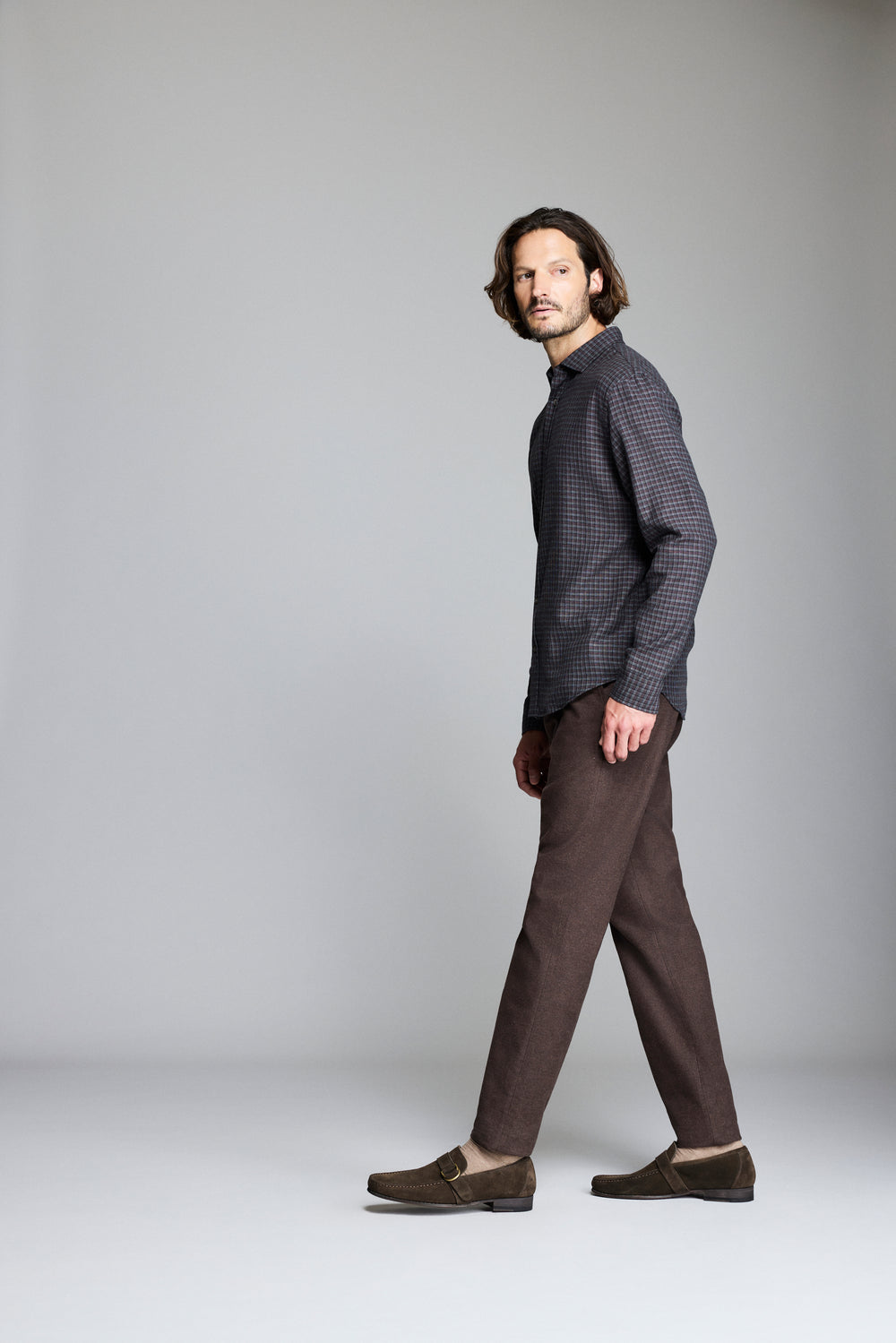 Man wearing a patterned shirt and brown pants on a plain background