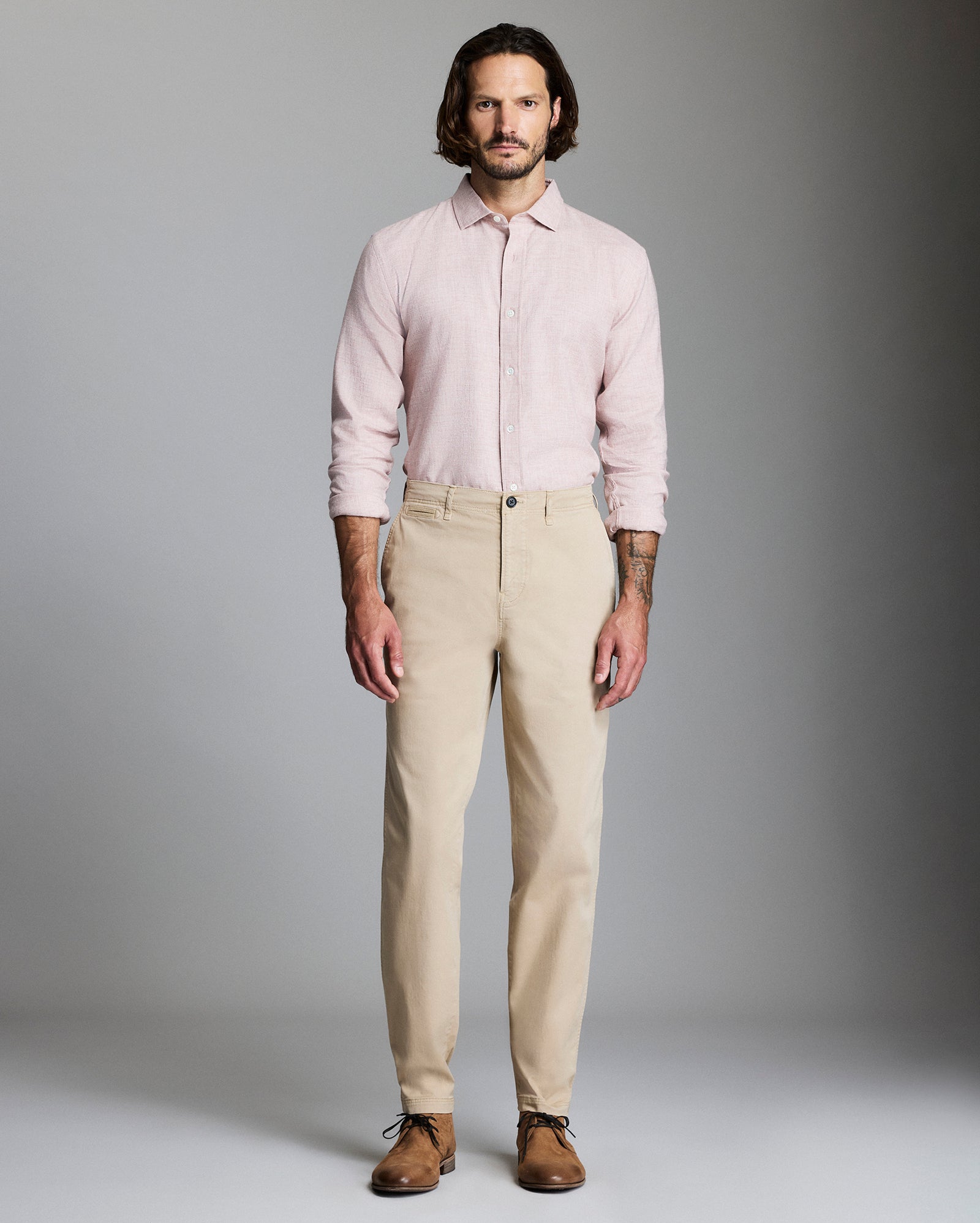 Man wearing a light pink shirt and beige pants against a gray background
