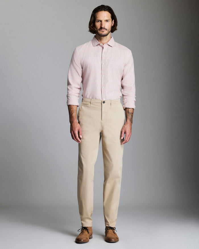 Man wearing a light pink shirt and beige pants against a gray background
