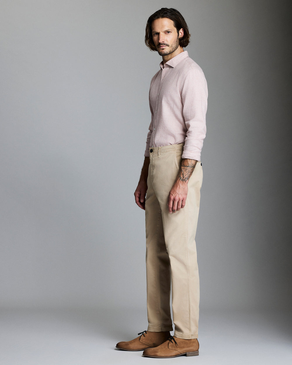 Man wearing a light pink shirt and beige pants against a gray background