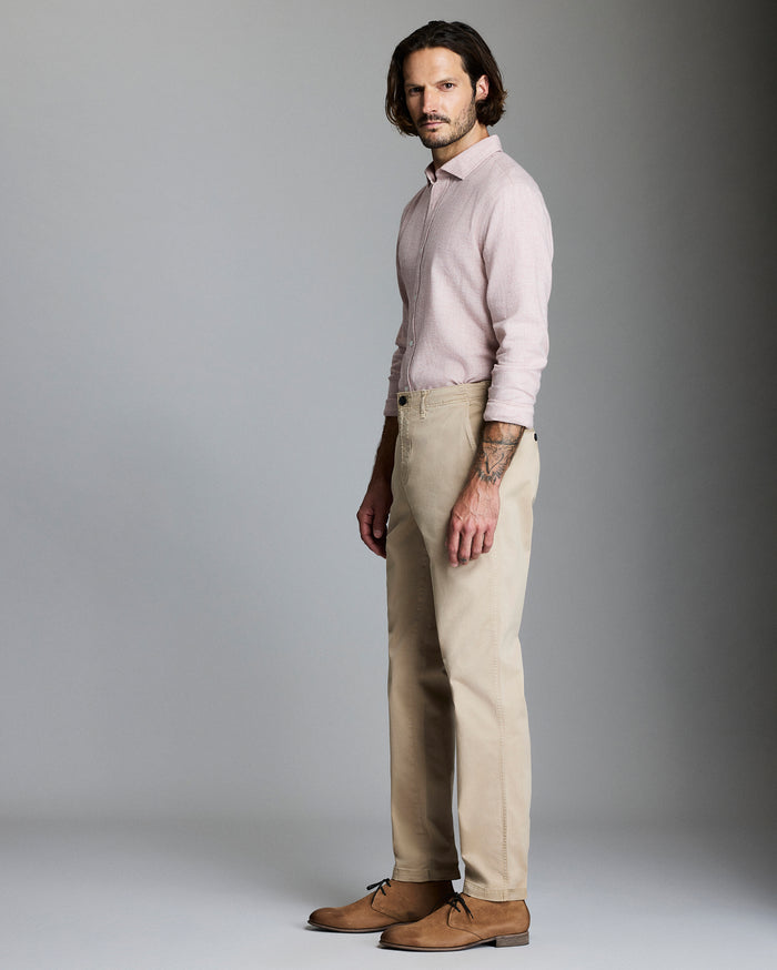 Man wearing a light pink shirt and beige pants against a gray background